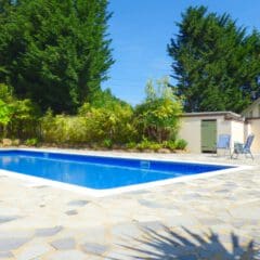 A rectangular outdoor swimming pool with clear blue water is surrounded by a stone patio. Perfect for relaxing, this space benefits from professional property management, ensuring it’s always ready for your next sunny getaway.