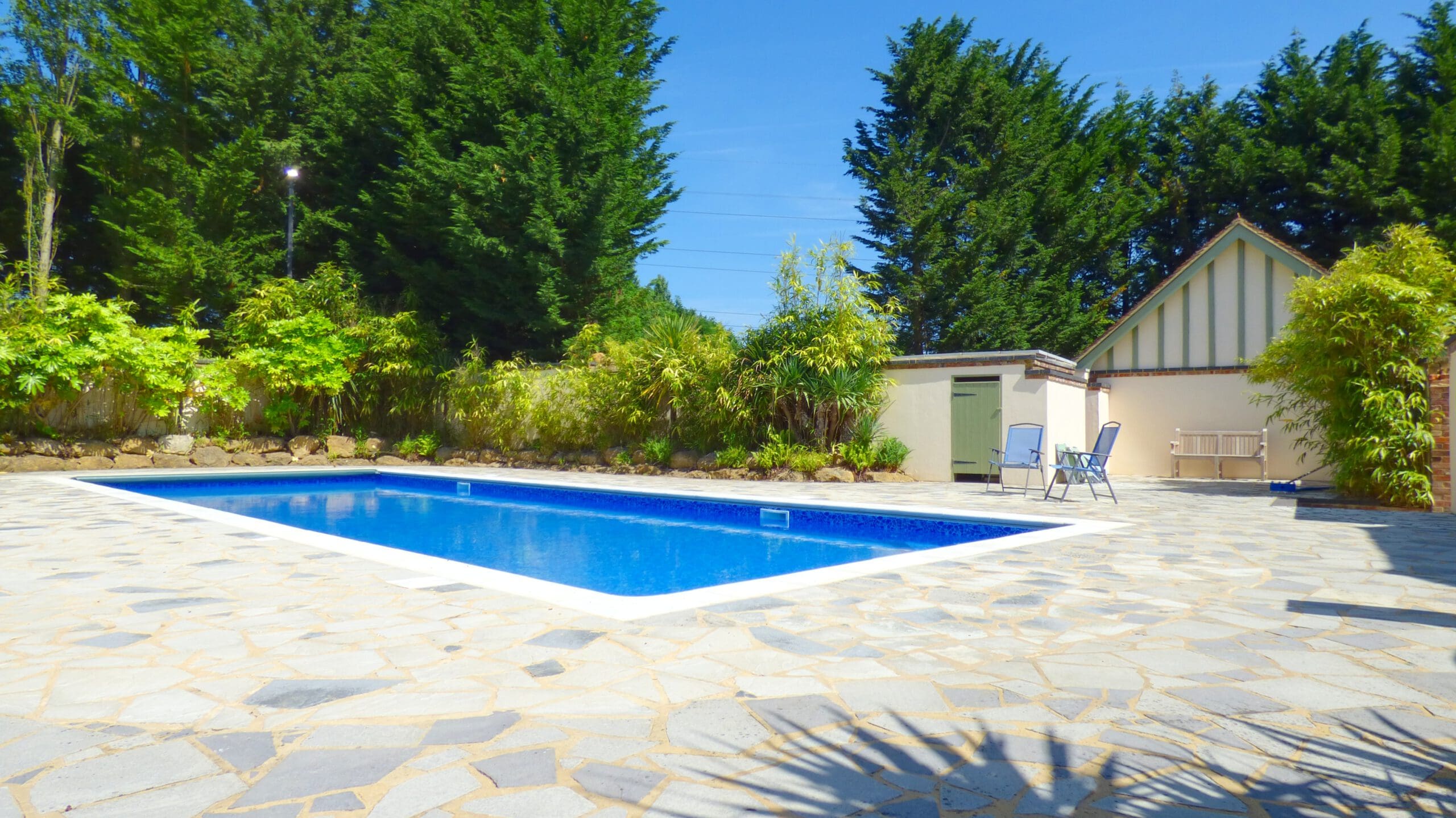 A rectangular outdoor swimming pool with clear blue water is surrounded by a stone patio. Perfect for relaxing, this space benefits from professional property management, ensuring it’s always ready for your next sunny getaway.