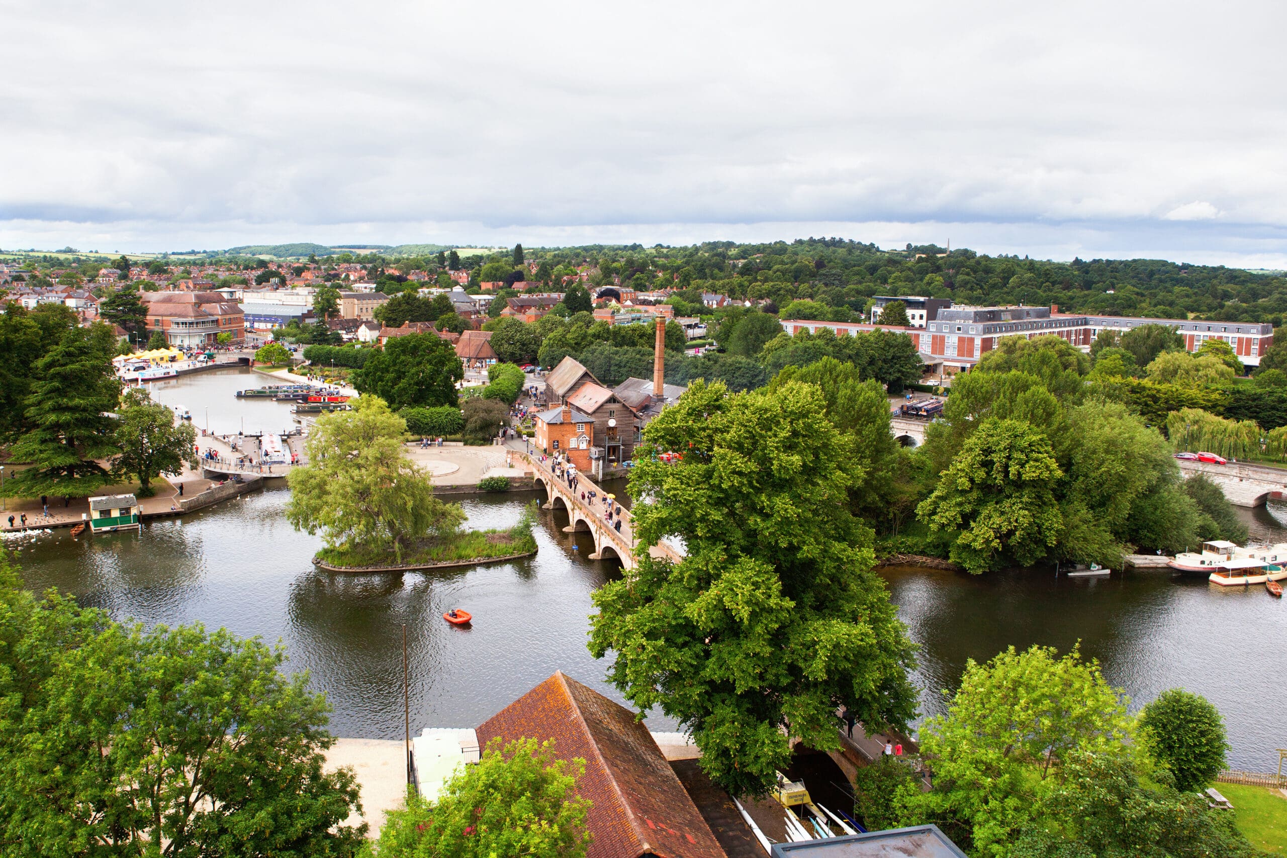 Aerial view of a riverside town with lush green trees, historic brick buildings, and a stone bridge—perfect for those seeking Fully Managed Holiday Lets or second home services in this vibrant community.