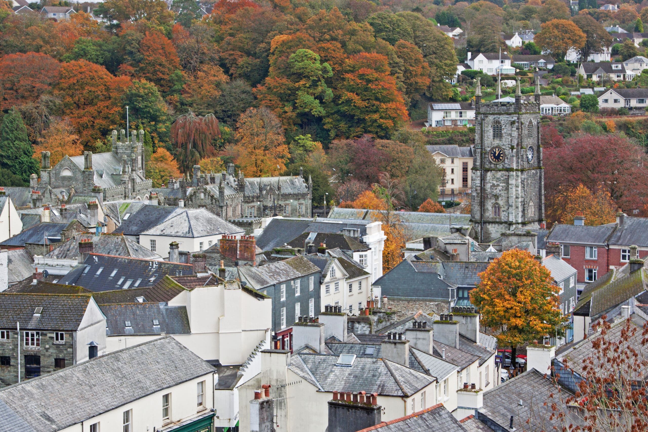 A view of a small town with slate-roofed houses, a prominent church tower with a clock, and trees in autumn colors in the background—ideal for fully managed holiday lets and seamless property management.